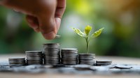 Growing plant on stacks of silver coins with hand adding money, representing financial growth, investment returns and sustainable business development.