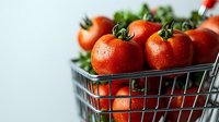 Fresh ripe red tomatoes with water drops in metal shopping basket on light background, selective focus, healthy organic produce for cooking.