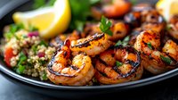 Grilled shrimp skewers with charred marks served on black plate with quinoa salad, fresh herbs, tomatoes and lemon wedges. Close up view of seafood dinner.