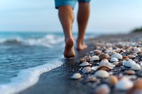 Bare feet walking on pebble beach along ocean shore with gentle waves washing up on stones, creating peaceful summer vacation atmosphere.