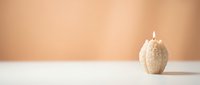Minimalist beige textured candle burning on white surface against warm peach background for spa relaxation home decor and wellness lifestyle concepts.