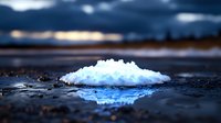 White crystalline salt pile on dark wet surface reflecting blue light against dramatic stormy sky background, natural mineral extraction concept.