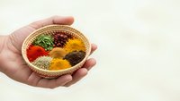 Hand holding wicker basket filled with colorful ground spices including turmeric, paprika, herbs and seasonings for cooking and culinary arts.