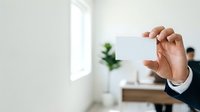 Businessman holding blank white business card in modern office environment with natural light and green plant decoration.