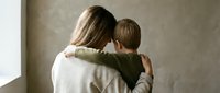 Mother embracing young son in warm hug showing unconditional love and family bond in cozy home setting with natural lighting creating intimate moment.