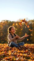 Happy young Hispanic girl throwing autumn leaves in air while sitting outdoors during golden hour sunset with warm sweater and jeans.