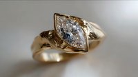 Elegant marquise diamond engagement ring in yellow gold setting with unique twisted band design and delicate leaf-inspired details, showcasing brilliant clarity and cut.