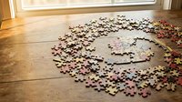 Unfinished jigsaw puzzle scattered on wooden floor near window with warm natural light creating cozy indoor atmosphere for leisure activity and problem solving.