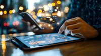 Person using digital tablet at night with glowing bokeh lights in background, finger touching screen displaying business analytics data and charts.