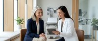 Two professional women having friendly business meeting in modern office setting with tablet and natural lighting.