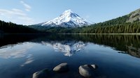 Majestic snow-capped mountain peak reflecting in calm lake waters with evergreen forest shoreline and rocks in foreground creating serene wilderness landscape.