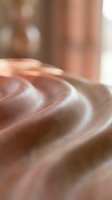Close-up of smooth flowing silk fabric with soft folds and gentle curves in warm beige tones creating elegant textile background for luxury fashion design.