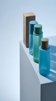 Luxury skincare cosmetic bottles in blue and green tones with wooden caps arranged on white geometric display for spa and beauty branding.