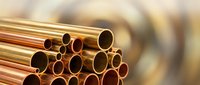 Stack of shiny copper pipes with golden metallic surface for plumbing, construction and industrial manufacturing applications on blurred background.
