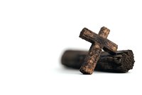 Rustic wooden cross leaning against dark log on white background, symbolizing faith, religion, and spiritual contemplation.