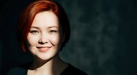 Young Caucasian woman with red hair smiling confidently in professional portrait with dramatic lighting and dark background for business content.