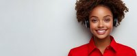 Young African American woman with curly hair wearing red shirt and wireless headphones smiling against light gray background with copy space.