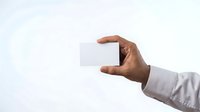 Male hand with medium-dark skin tone wearing white shirt sleeve holding blank white card horizontally against neutral background for business, corporate, or marketing design use.