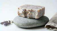 Handmade soap bar with natural ingredients and lavender buds resting on smooth stone, displayed with linen cloth for spa, wellness, and skincare product marketing.