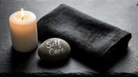 Self care stone with candle and folded dark towel on slate background, wellness and mindfulness concept for spa and relaxation.