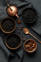 Copper teapot and bowls with loose black tea leaves, star anise and cinnamon sticks on dark background, moody food photography composition for tea ceremony.