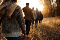 Group of people walking in line through autumn forest path during golden sunset, creating atmospheric silhouettes against warm backlight in nature.