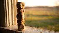 Wooden carved tiki totems stacked on windowsill during golden hour sunset with blurred landscape background for home decor and cultural art concepts.