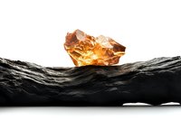 Raw amber crystal glowing with golden light rests on dark textured stone surface against white background, isolated mineral specimen for jewelry design.