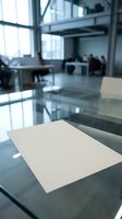 Empty white paper on glass desk in modern office with blurred colleagues working in background, suitable for business mockups and corporate presentations.