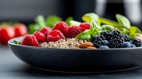 Fresh berries, nuts and seeds in black ceramic bowl on dark background. Healthy breakfast ingredients with raspberries, blackberries, blueberries and almonds.