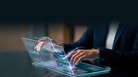 Businessperson in dark suit working on transparent laptop displaying digital holographic interface with glowing data visualization and circuit patterns for technology and innovation concepts.