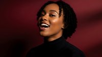 Young African American woman with natural curly hair laughing joyfully in black turtleneck against red background for lifestyle and portrait photography.