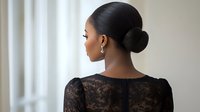 Young African American woman with elegant hair bun wearing black lace dress, photographed from behind against light window background, showcasing classic beauty and style.