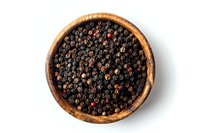 Black peppercorns in rustic wooden bowl on white background, overhead view. Perfect for cooking, seasoning, and culinary design projects, isolated food ingredient photography.
