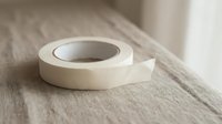 White adhesive tape roll on wooden surface for crafting projects and office supplies.