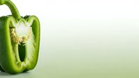 Fresh green bell pepper cut in half showing seeds and interior on gradient background with copy space for healthy cooking and nutrition concepts.