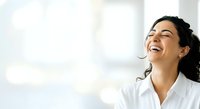 Young woman with dark hair and East Asian ethnicity wearing white business shirt, smiling with joy and confidence in bright office environment with blurred background, suitable for corporate and professional use.