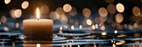 Glowing candle on reflective surface with golden bokeh lights creating peaceful atmosphere. Water droplets add serene ambiance in dark setting.