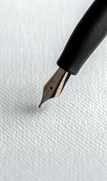 Fountain pen nib close-up on textured white paper background, showing detailed metallic tip and black holder for writing and calligraphy projects.