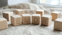 Wooden alphabet blocks spelling EMDR on soft bedding near window with natural light for therapy and mental health concepts.