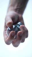 Hand holding transparent glass sphere crystal ball with soft focus background for fortune telling divination and spiritual practices.