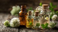Natural herbal essential oils in glass bottles with fresh clover flowers and green leaves on rustic wooden surface for aromatherapy and wellness.