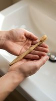 Hands holding bamboo toothbrush in bathroom setting promoting sustainable oral care and eco-friendly dental hygiene practices for environmental wellness.