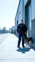 Professional security guard with trained German Shepherd dog patrolling industrial warehouse district for safety and protection services.