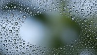 Water droplets on glass surface creating natural condensation pattern with blurred green background for fresh morning dew concept.