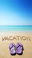 Vacation written in sand on sunny tropical beach with purple flip flops, turquoise sea, and sailboat on horizon. Summer travel concept.
