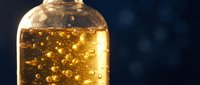 Bottle of golden sparkling liquid with bubbles rising against dark background, suitable for beverage, cosmetics, or luxury product marketing.