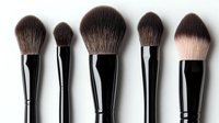 Professional makeup brushes set with soft brown and beige bristles and black handles arranged in row on white background, isolated cosmetic tools for beauty artists.