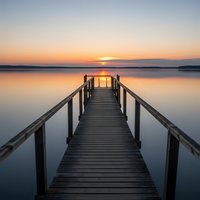 Wooden pier extending into calm lake at golden sunset with peaceful reflections and serene atmosphere for meditation and relaxation concepts.