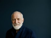 Senior man with white beard and gray hair, Caucasian ethnicity, wearing dark navy sweater against dark teal background. Professional portrait suitable for business, healthcare, corporate websites, and editorial use.